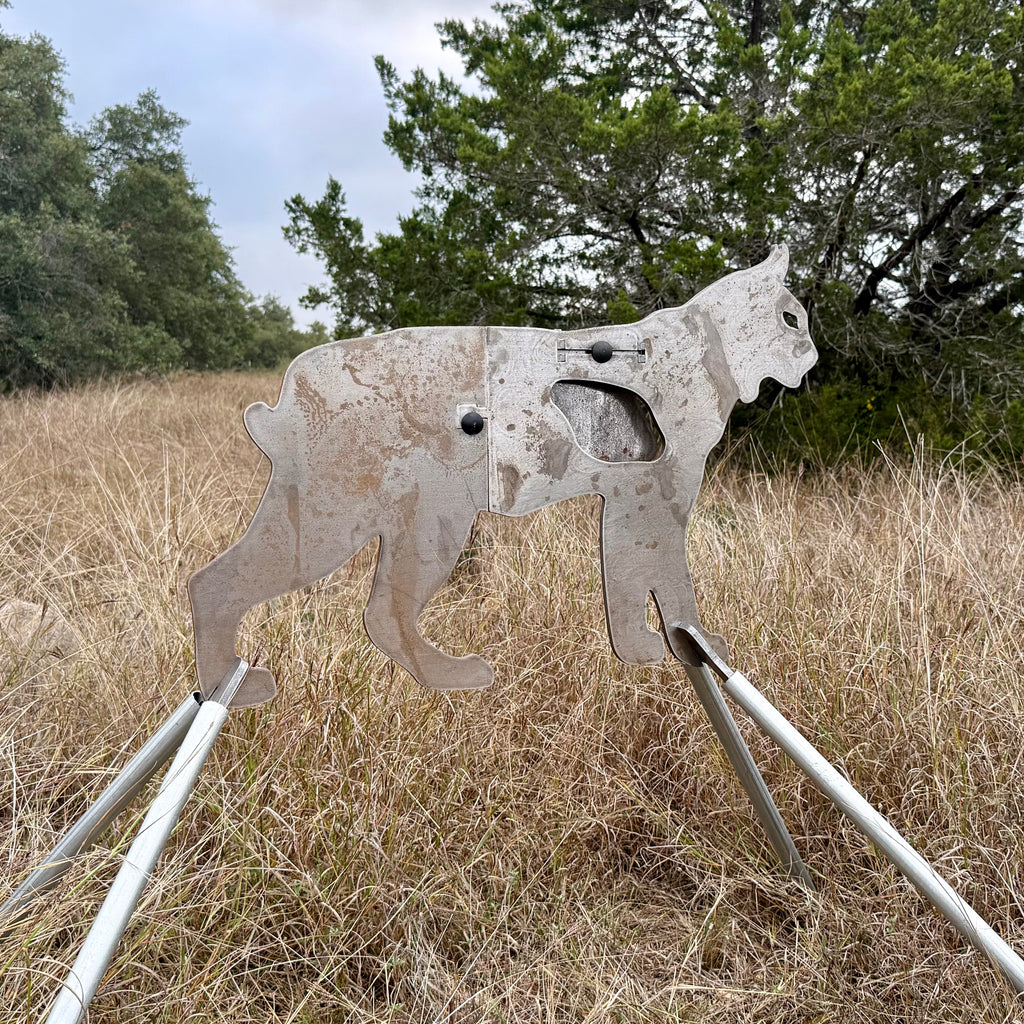 AR500 Steel Bobcat target on a stand in a grassy outdoor area with trees in the background