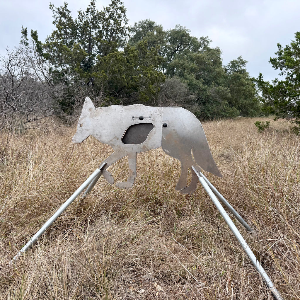 AR500 Steel Coyote target on a stand in a grassy outdoor area with trees in the background