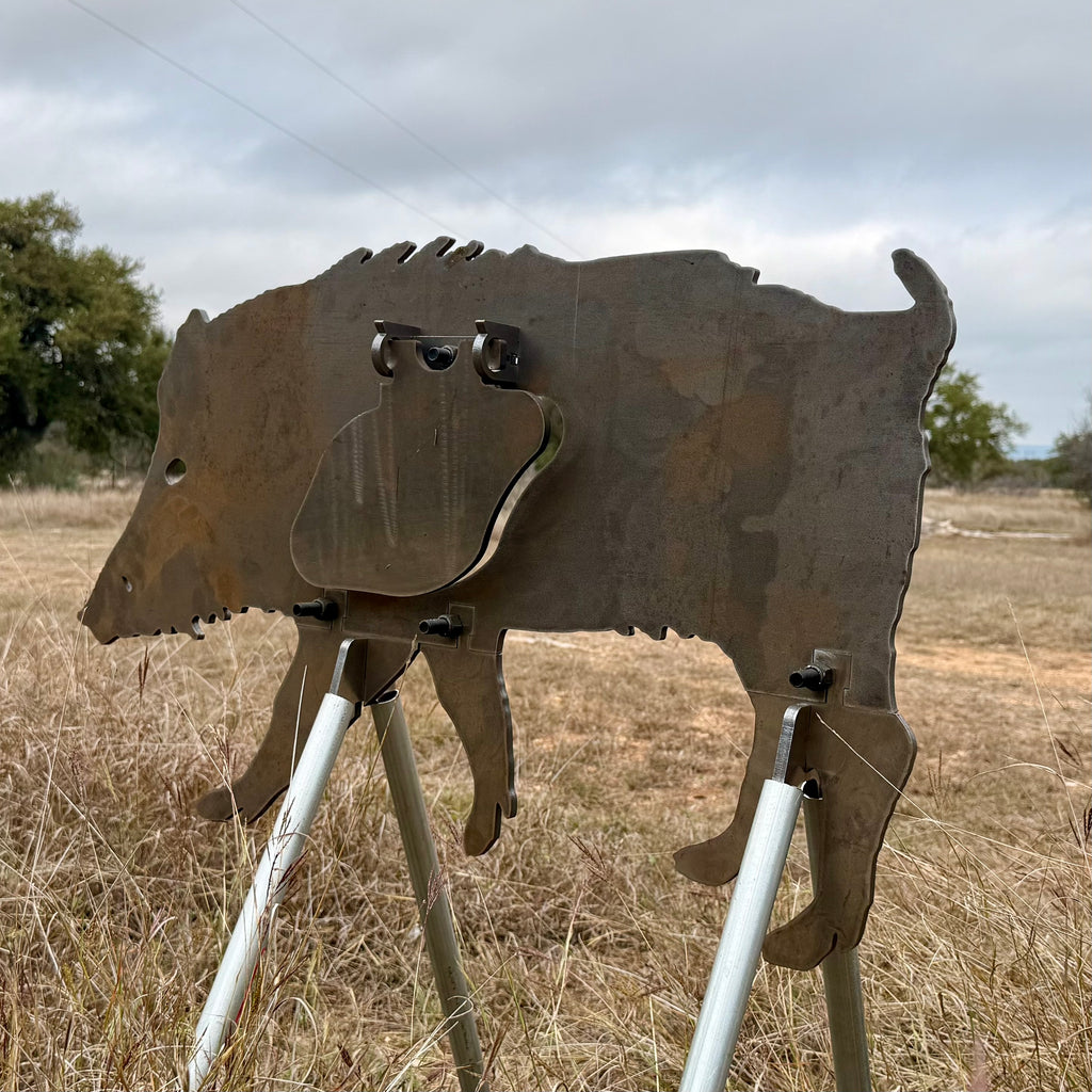 AR500 Steel Feral Hog target on a stand in a grassy outdoor area with trees in the background