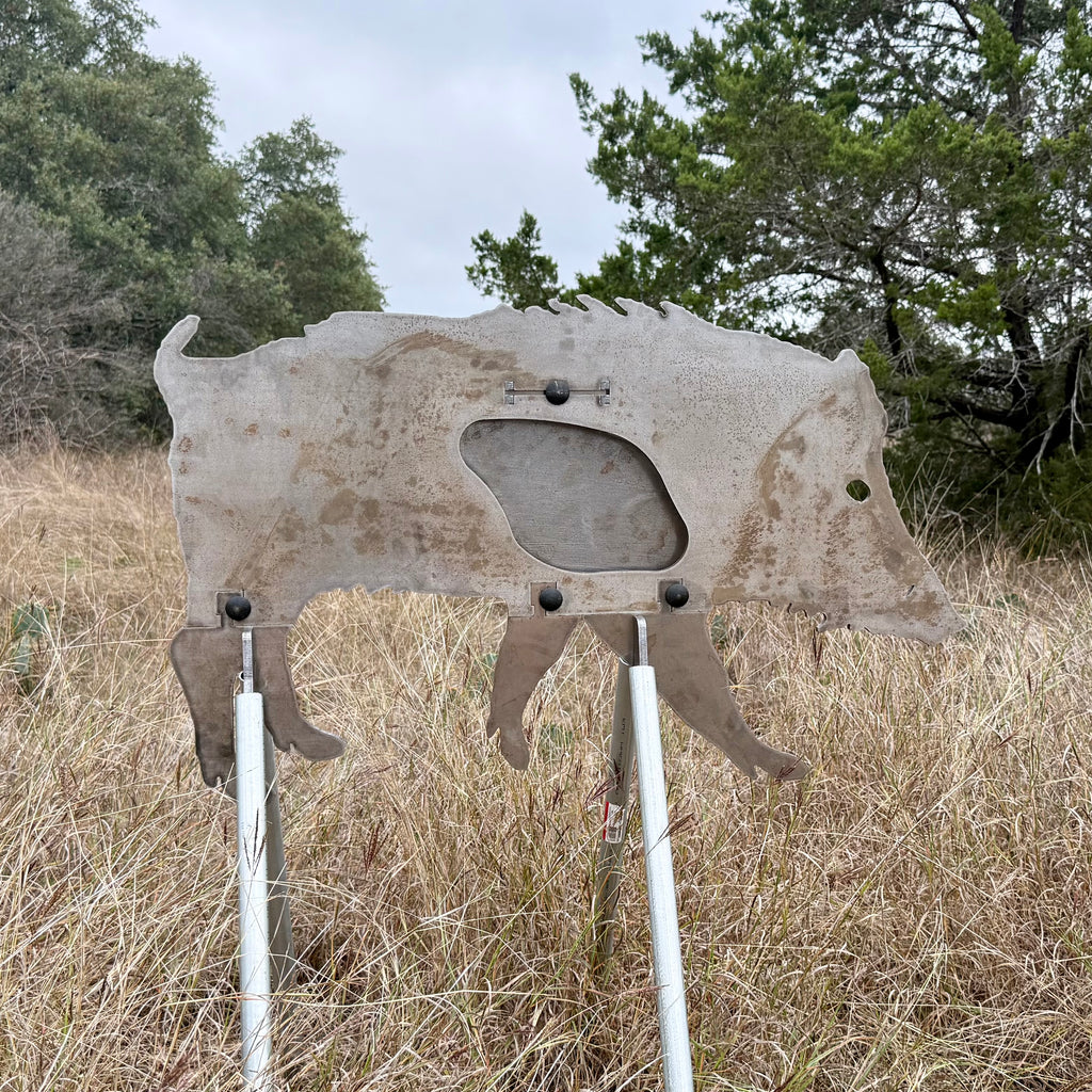AR500 Steel Feral Hog target on a stand in a grassy outdoor area with trees in the background